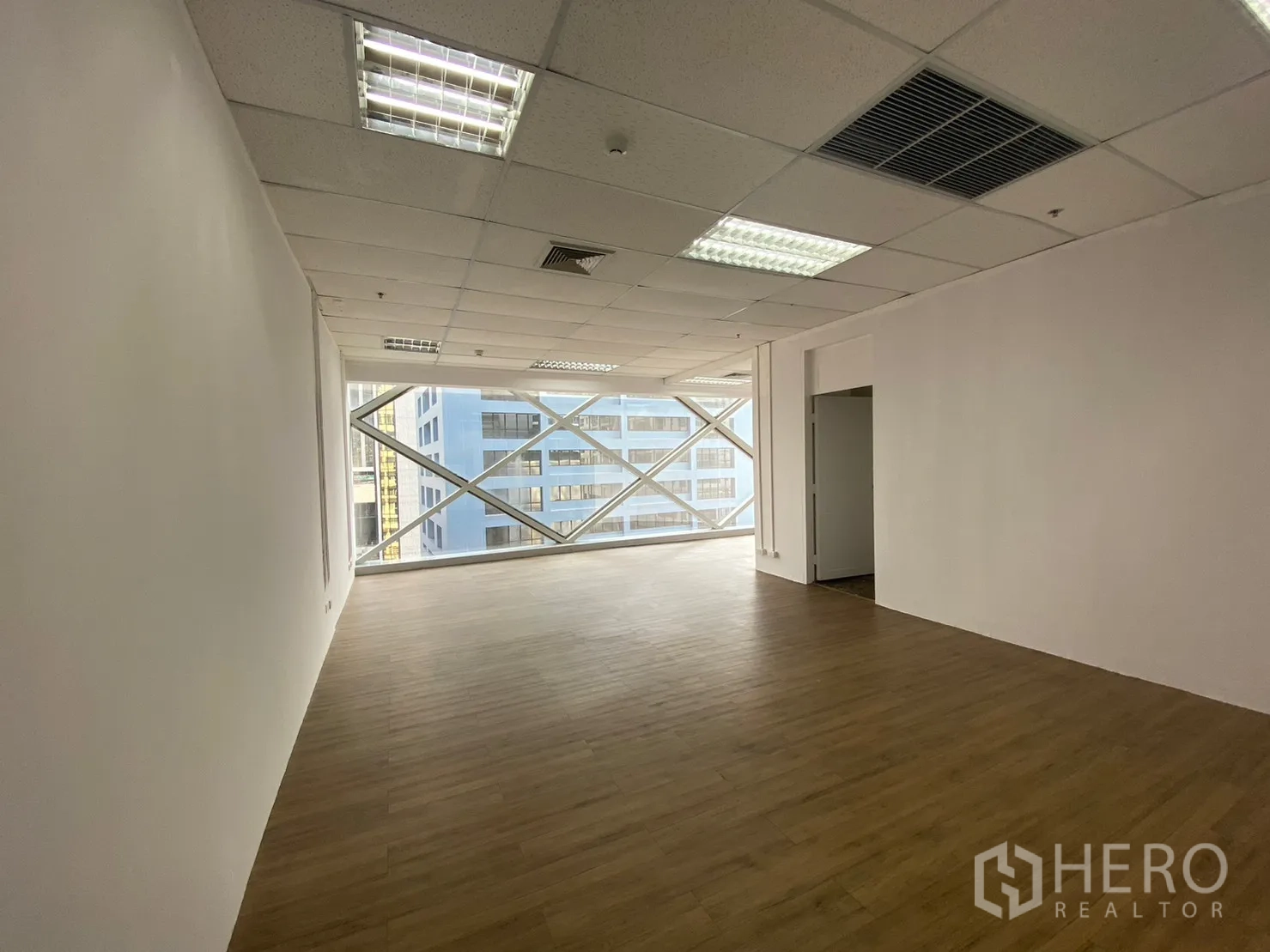 办公空间 出租在Watthana, Bangkok - 明亮的开放式办公室，木纹地板、格栅天花灯光与带X形立面的大窗，城市景观。