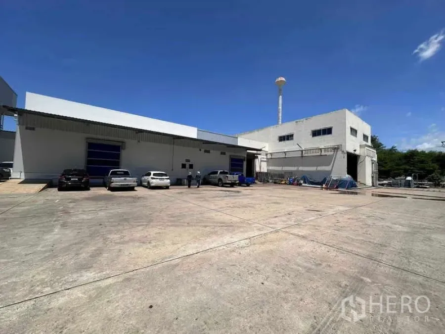 Factory for rent - Exterior of factory buildings with blue roller doors, large concrete yard, and parking under a clear blue sky.