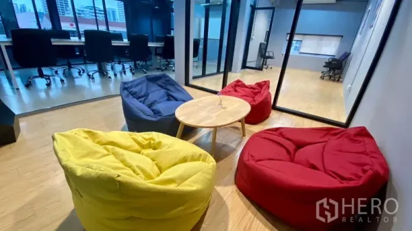 Office Space for rent in Sathon, Bangkok - Colorful beanbag lounge with a round coffee table beside glass-partitioned offices in a modern workspace.