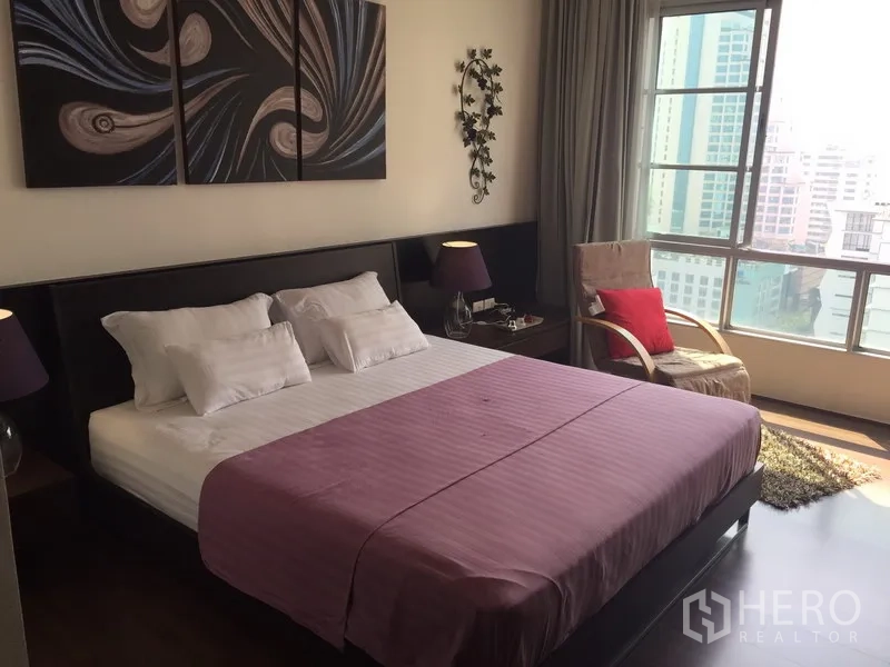 Condominium for rent in Khlong Toei, Bangkok - Master bedroom with wide windows showing city views and a lounge chair.