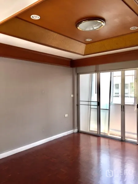 Townhouse for rent in Watthana, Bangkok - Bright living area with parquet floor, recessed ceiling and sliding glass doors to a balcony.