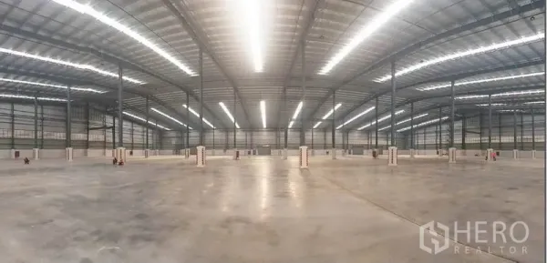 Factory for rent in Mueang Rayong, Rayong - Panoramic view of an expansive warehouse floor with bright linear lighting and a grid of steel columns.