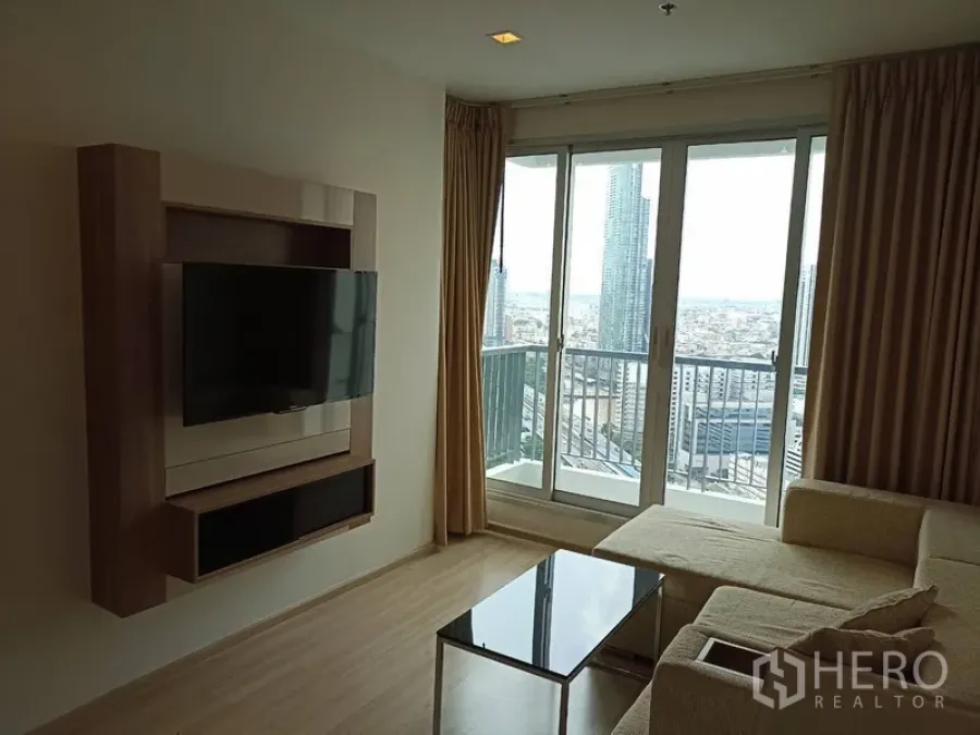 Condominium for rent or sale in Sathon, Bangkok - Bright living room with L-shaped sofa, wall-mounted TV and balcony overlooking the Bangkok skyline.