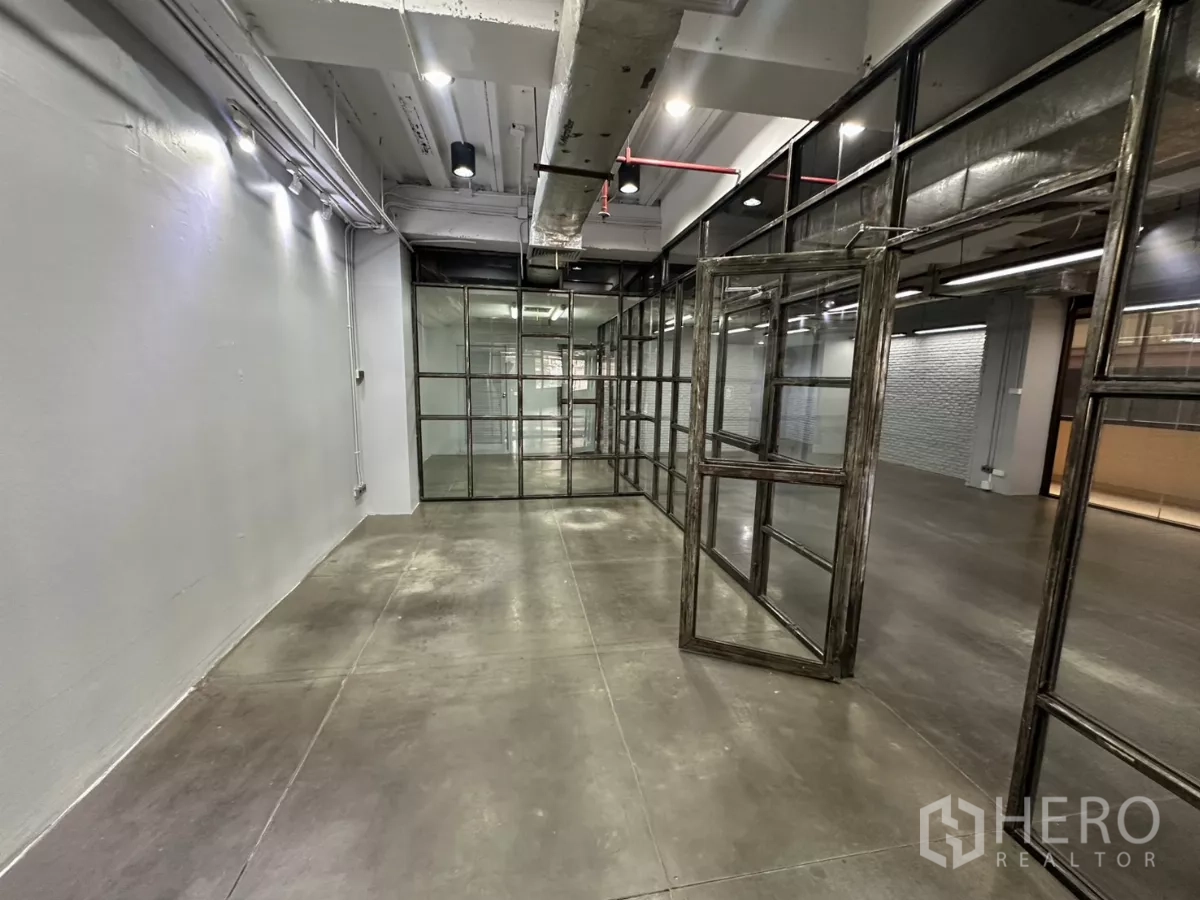 Office Space for rent - Narrow room with pivoting glass doors and exposed ceiling pipes.
