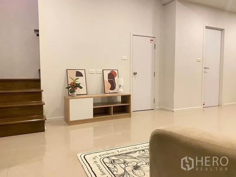 Townhouse for rent in Prawet, Bangkok - Living area corner with TV console, decorative artwork and wooden staircase.