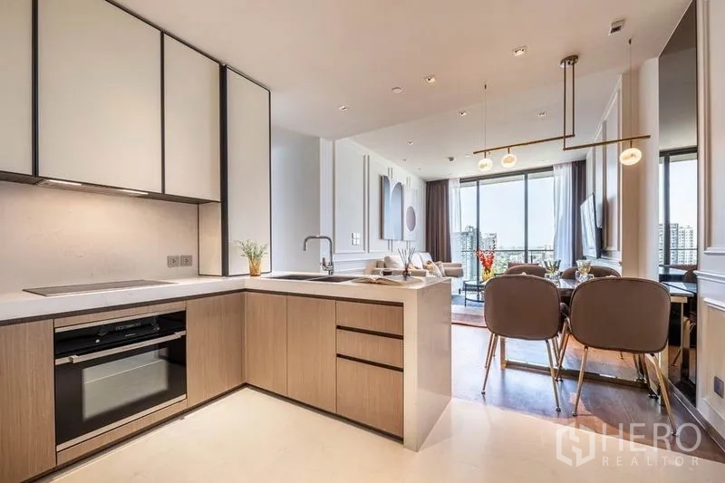 Condominium for rent in Khlong Toei, Bangkok - L-shaped kitchen with built-in oven beside dining set and city view.