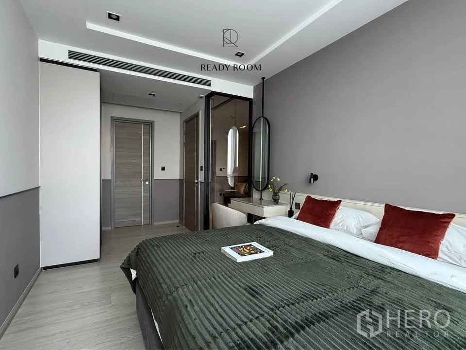 Condominium for rent in Khlong Toei, Bangkok - Modern bedroom with a large bed, rust accent pillows, built-in vanity, and glass partition.