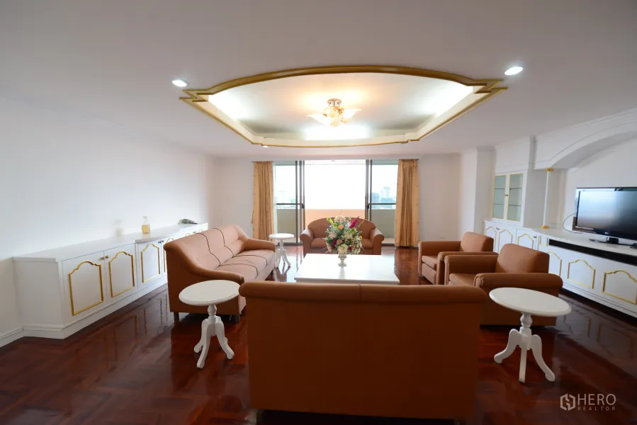 Condominium for rent or sale in Watthana, Bangkok - Spacious condo living room with parquet floors, brown sofa set, built-in cabinetry and balcony city view