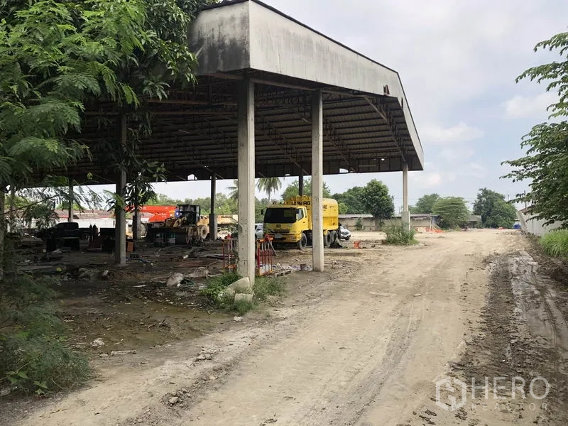 Factory for rent in Phra Nakhon Si Ayutthaya - Covered bay with concrete columns sheltering trucks next to a wide dirt access road.