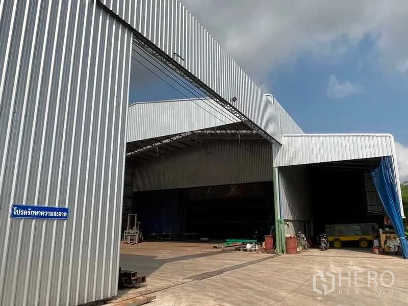 工厂 出售在Nikhom Phatthana, Rayong - 厂房宽阔入口与金属滑门，前方为大型混凝土堆场。