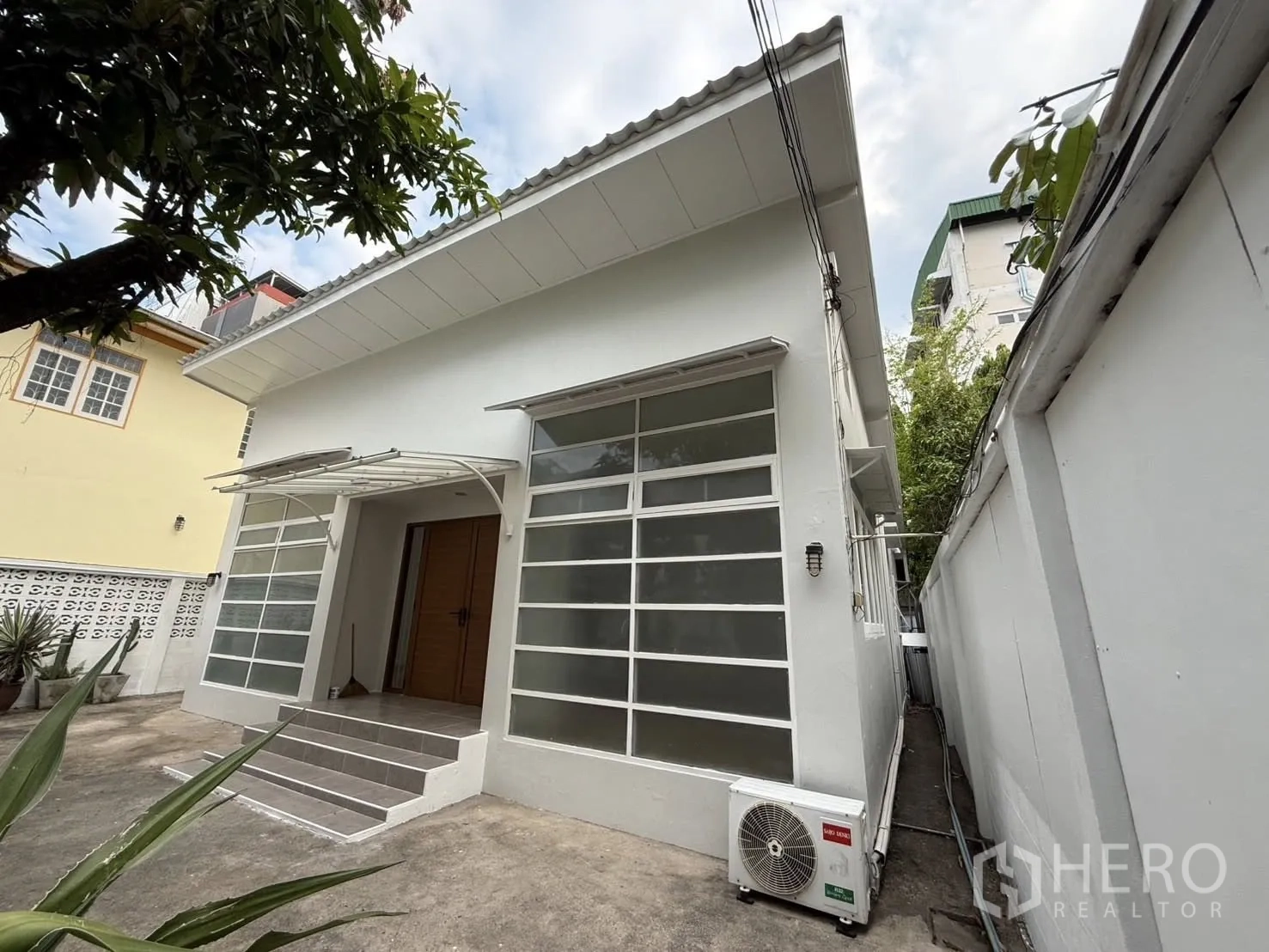 Detached House for rent in Khlong Toei, Bangkok - Side view of a single-storey house with steps to the entrance and an outdoor AC unit.