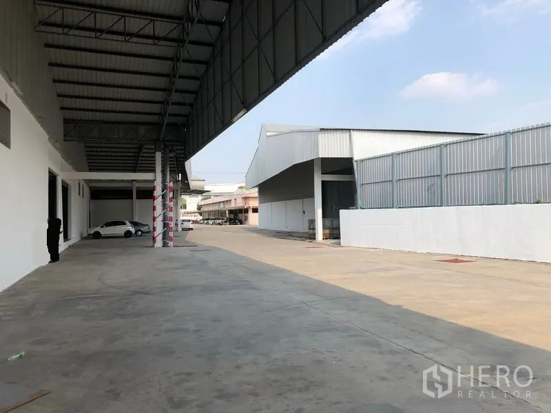 货栈 出租在Pak Kret, Nonthaburi - 仓库侧边带雨棚的装卸区，混凝土硬化场地宽阔并可停车。