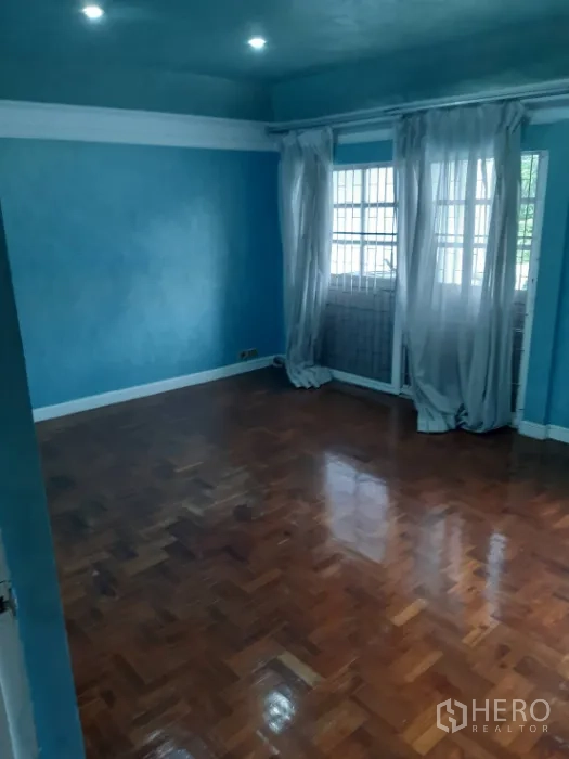 Townhouse for rent in Khlong Toei, Bangkok - Room with blue walls, parquet flooring and sheer curtains at wide windows.
