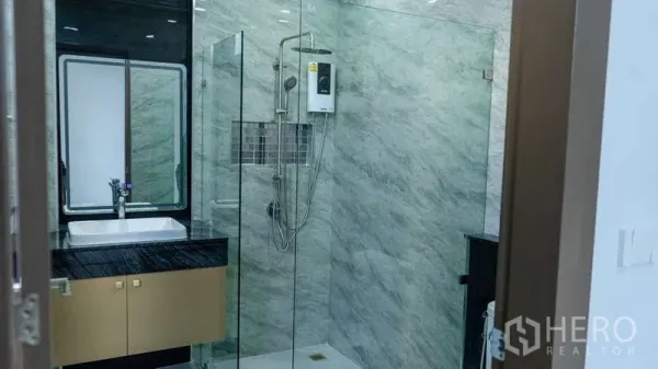 Detached House for rent or sale in Suan Luang, Bangkok - Glass-enclosed shower with water heater and stone-effect wall tiles beside a vanity