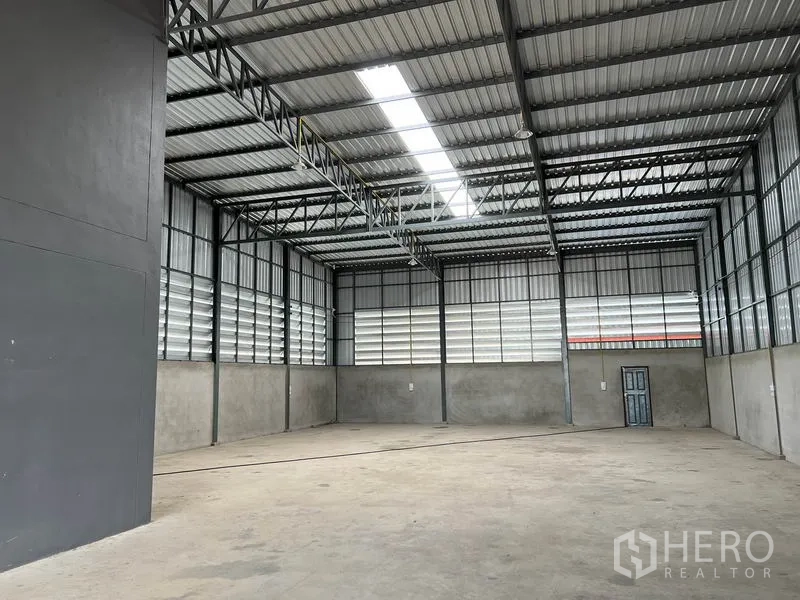 Warehouse for rent in Lam Luk Ka, Pathum Thani - Bright high-bay storage area with concrete floor and ventilation louvers along the walls.