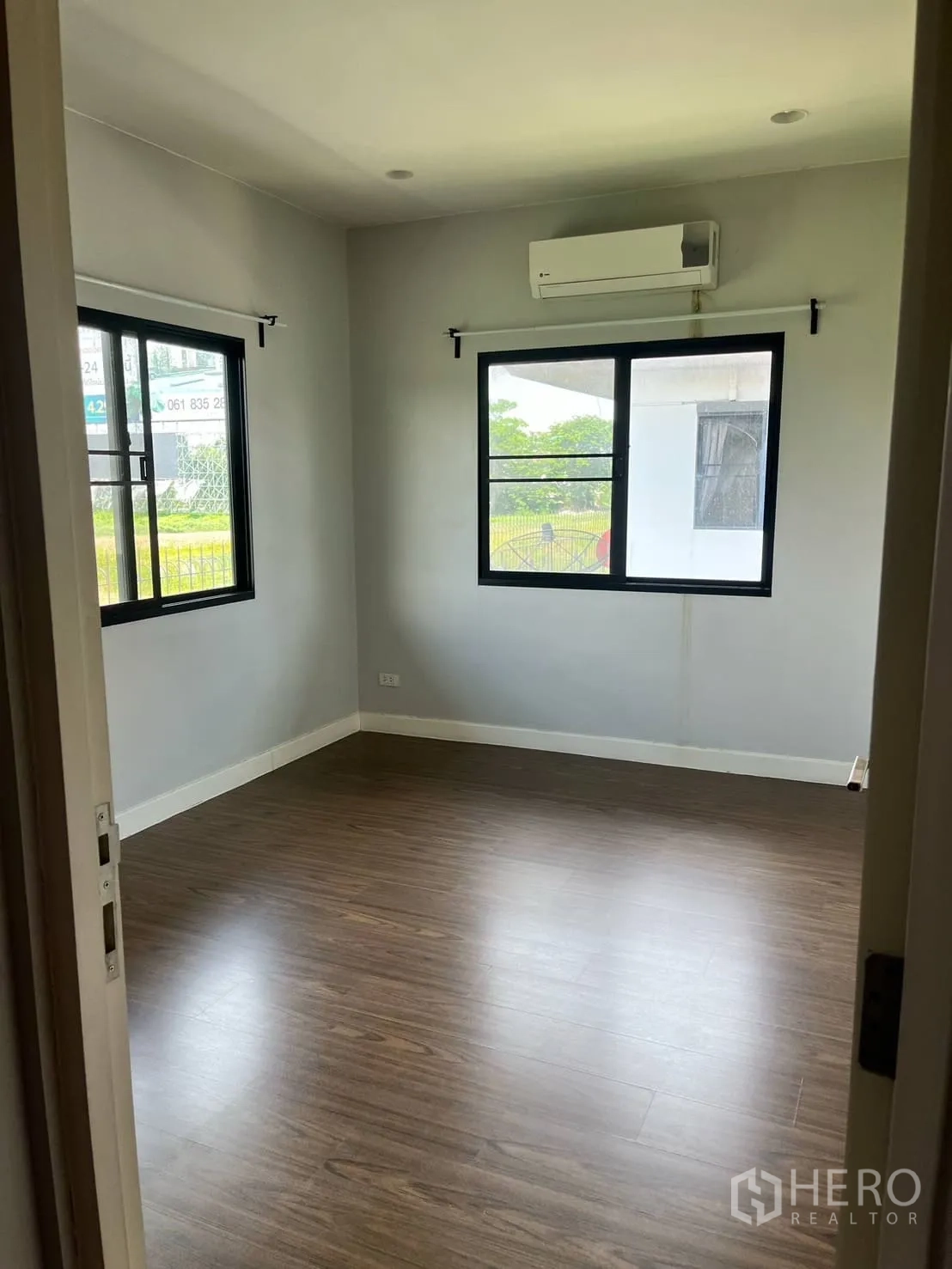 Detached House for rent or sale in Lam Luk Ka, Pathum Thani - Air‑conditioned bedroom with two windows and wood laminate flooring.