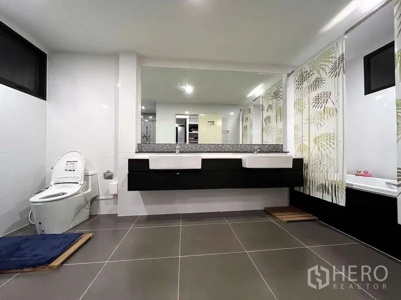 Detached House for sale in Prawet, Bangkok - Oversized bathroom with double vanity, bathtub behind patterned curtains, and gray floor tiles.