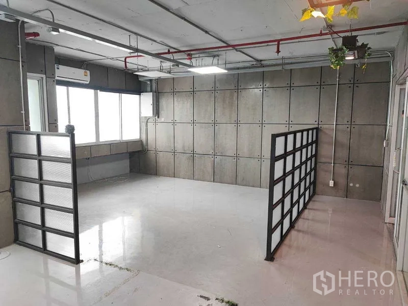 Office Space for rent in Watthana, Bangkok - Open-plan office area with two black-framed dividers, exposed pipes and hanging greenery.