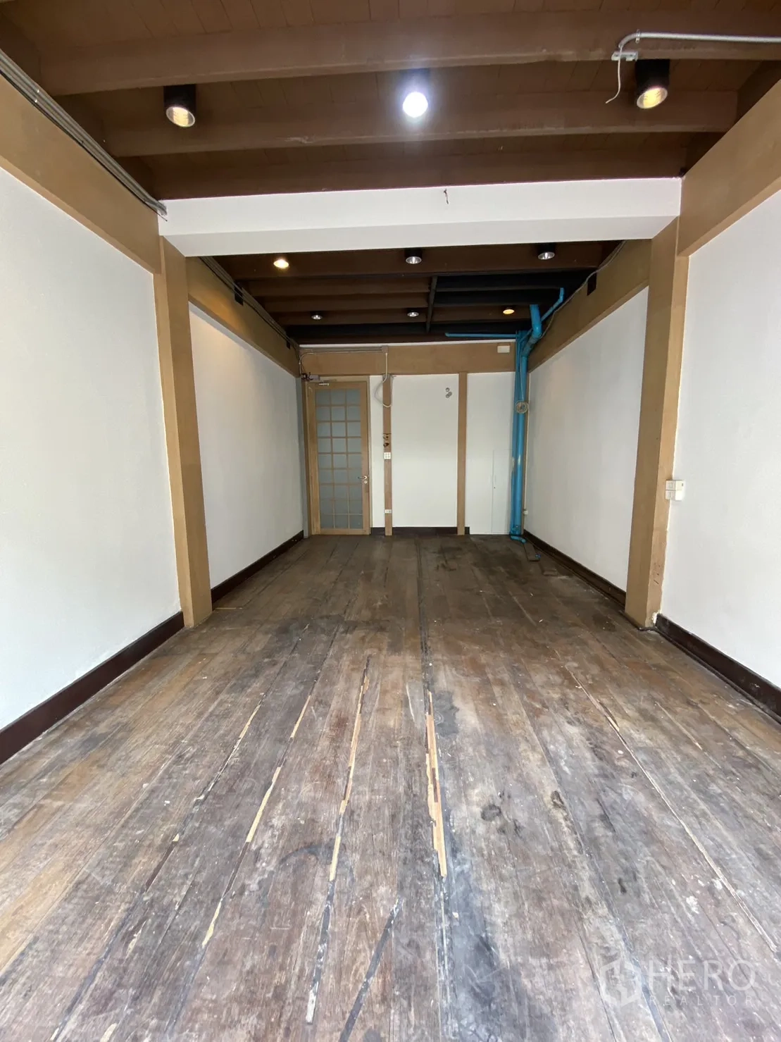 Shophouse for rent - Upper-floor room with exposed beams, white walls and worn wooden floorboards.