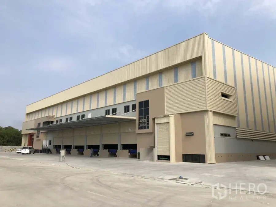 Factory for rent or sale in Samut Prakan - Modern factory exterior with multiple dock-level loading bays, canopy, and a wide concrete yard.