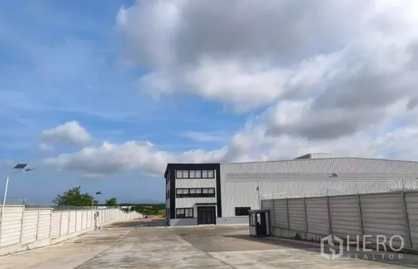 Warehouse for rent in Si Racha, Chon Buri - Large warehouse with attached office block, wide concrete driveway, high boundary wall, and solar light poles.