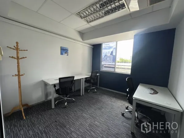 Office Space for rent in Watthana, Bangkok - Bright private office with a city-view window, three desks and a coat rack.