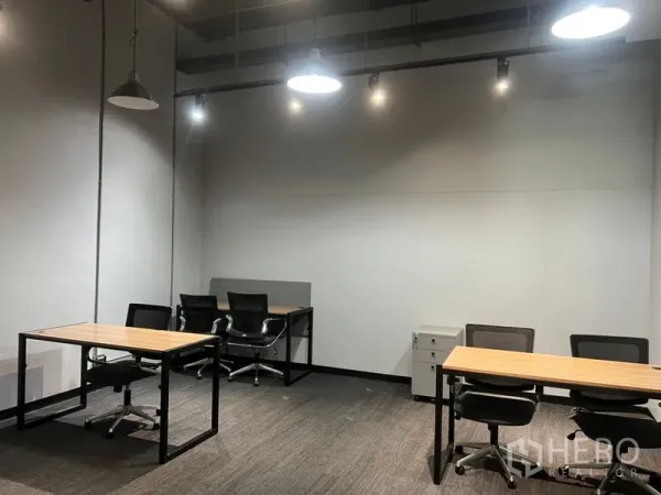 Office Space for rent - Compact furnished office showing wood-top desks, ergonomic chairs, white walls, ceiling cassette AC and spotlights.