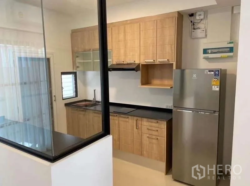 Townhouse for rent in Bang Phli, Samut Prakan - Compact kitchen with wood cabinets, black countertops, range hood and stainless fridge.