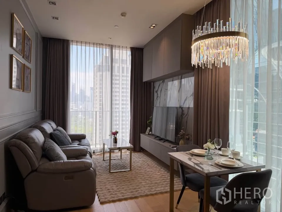 Condominium for rent in Pathum Wan, Bangkok - Bright living and dining area with floor-to-ceiling windows, city and park view, sofa, TV wall, and chandelier in a modern condo.