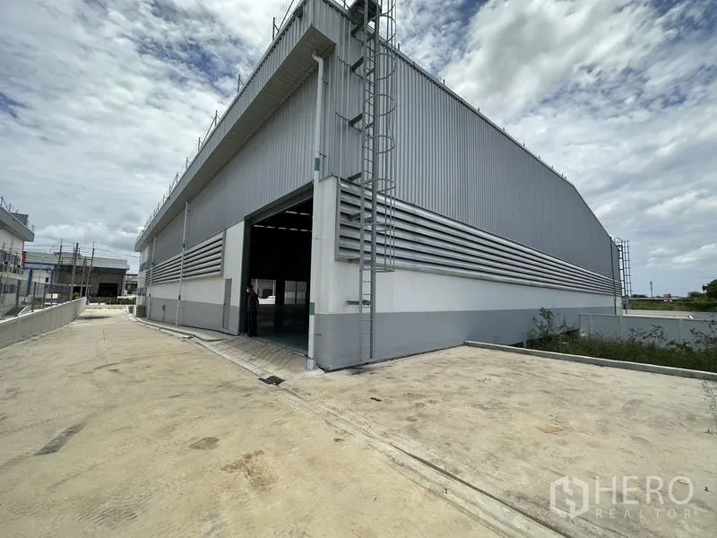 Factory for rent in Mueang Samut Prakan, Samut Prakan - Side view of the warehouse showing driveway, open roller door, and roof access ladders.