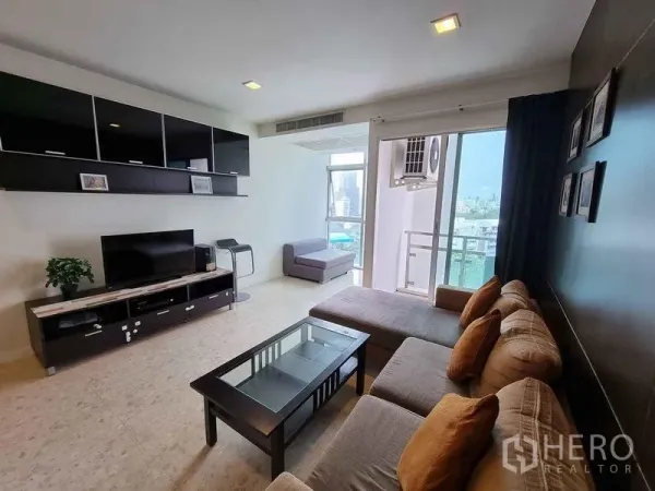 Condominium for rent in Khlong Luang, Pathum Thani - Bright living room at Nusasiri Grand Condo with L‑shaped sofa, TV console and balcony overlooking Bangkok skyline.