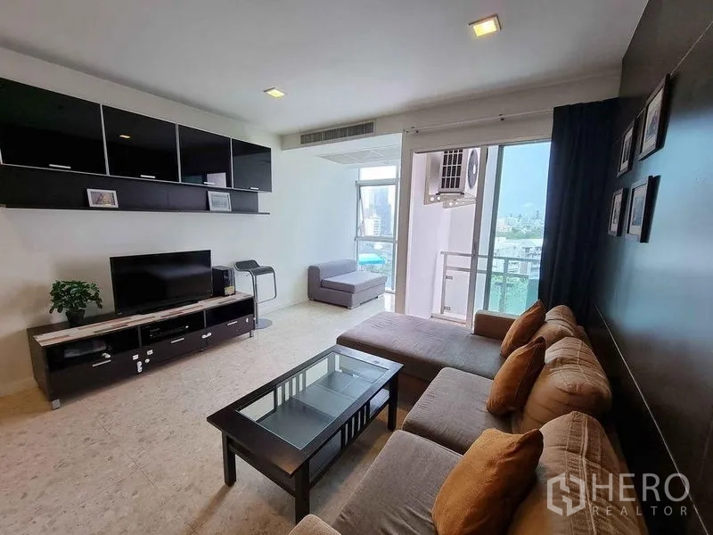 Condominium for rent in Khlong Luang, Pathum Thani - Bright living room at Nusasiri Grand Condo with L‑shaped sofa, TV console and balcony overlooking Bangkok skyline.