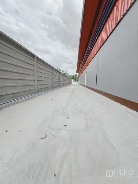 Warehouse for rent or sale in Khlong Luang, Pathum Thani - Narrow concrete service lane running along the warehouse and boundary wall with drainage points.