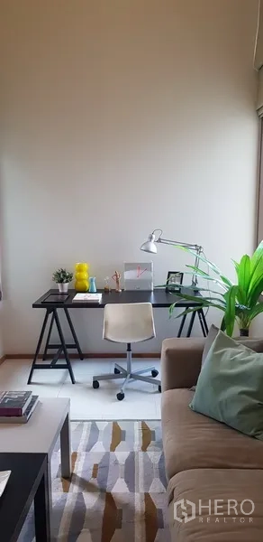 Condominium for rent in Khlong Toei, Bangkok - Home office nook next to sofa with plants and task lamp.