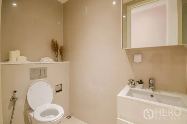Condominium for rent or sale in Watthana, Bangkok - Minimalist bathroom with wall-mounted toilet, vanity and neutral tiles.