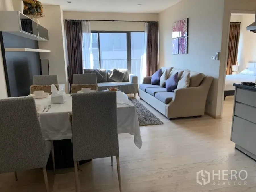 Condominium for rent in Khlong Toei, Bangkok - Open-plan living and dining area with four-seat table, sofas and balcony doors bringing natural light.