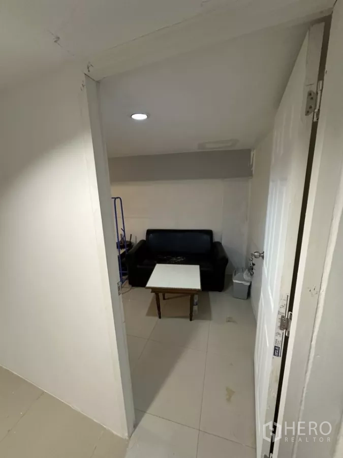 Retail Space for rent - Small back room with a black sofa and table under recessed ceiling lighting.