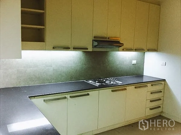 Townhouse for rent in Khlong Toei, Bangkok - Modern kitchen featuring long black countertop, gas cooktop, range hood and under‑cabinet lighting.