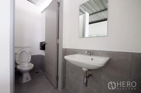 Office Space for rent in Khlong Toei, Bangkok - Clean modern restroom with gray tiles, toilet, wall-mounted sink and mirror.