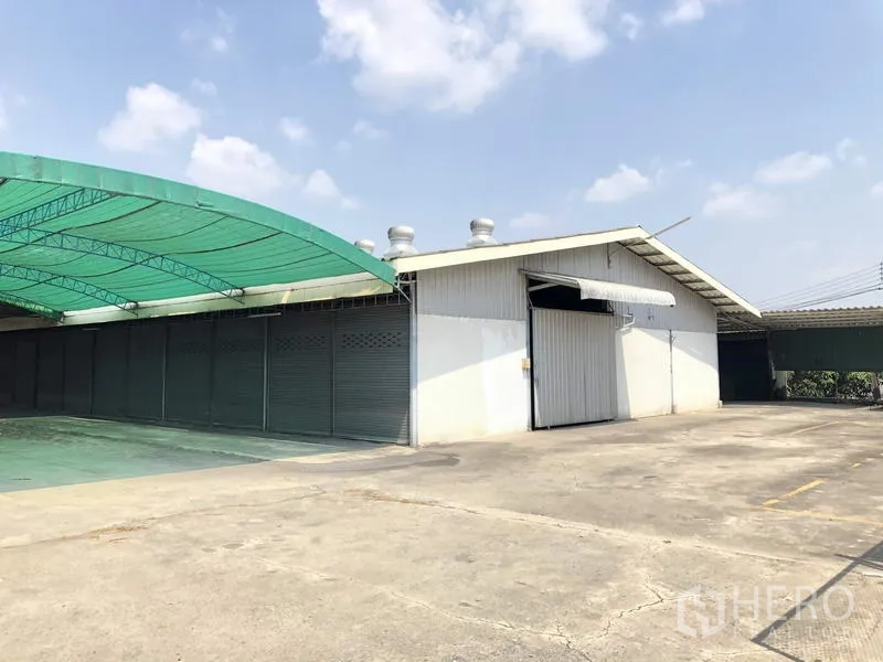 Warehouse for rent in Khlong Luang, Pathum Thani - Warehouse exterior with wide metal sliding door, roof ventilators and a broad concrete yard in Khlong Luang.