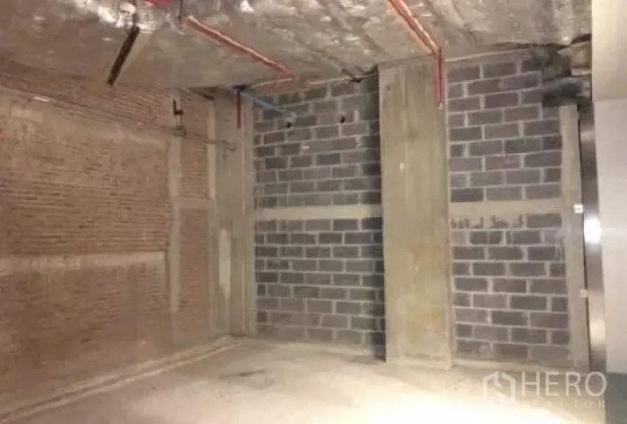 Retail Space for rent - Unfinished 76 sqm retail unit with exposed concrete ceiling, brick and block walls, and visible red piping.