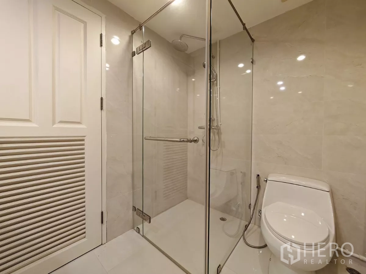 Condominium for rent in Pathum Wan, Bangkok - Contemporary bathroom with glass-enclosed shower and light tiles.