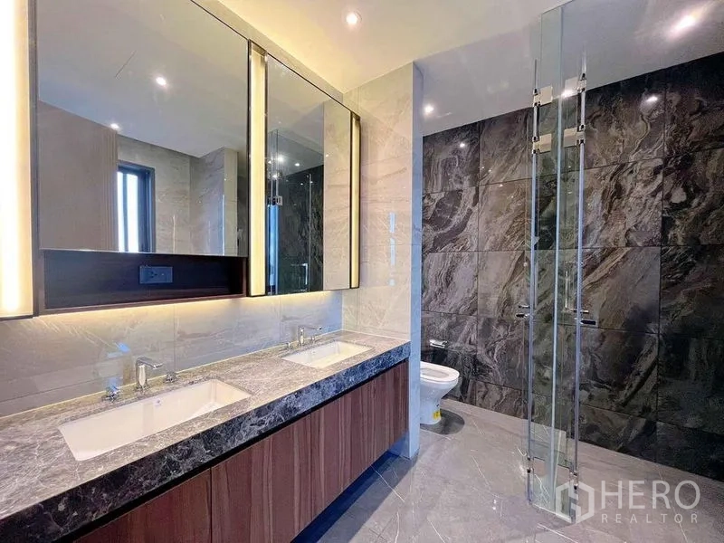 Detached House for sale in Bang Phli, Samut Prakan - Contemporary bathroom with double vanity, backlit mirrors, and a glass-enclosed shower against a dark stone wall.