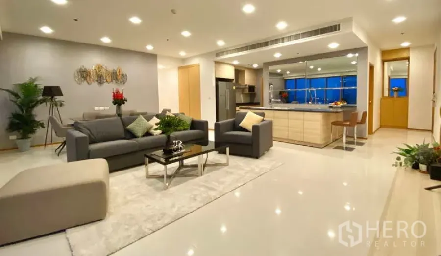 Condominium for rent or sale in Khlong Toei, Bangkok - Open-plan living room with grey sofas, recessed lighting and a large kitchen island.