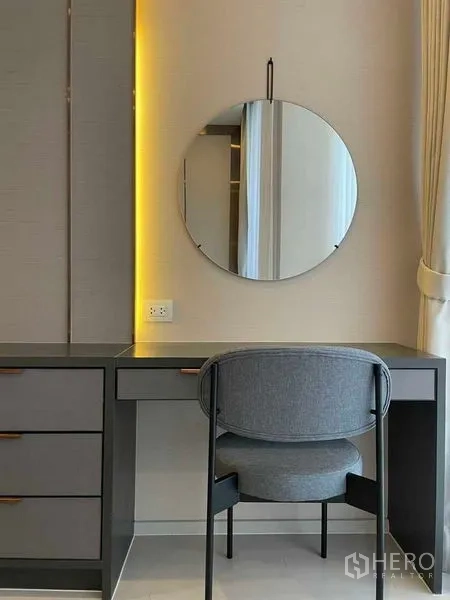 Condominium for rent in Pathum Wan, Bangkok - Work or vanity desk with a round mirror and warm backlighting beside the curtain.