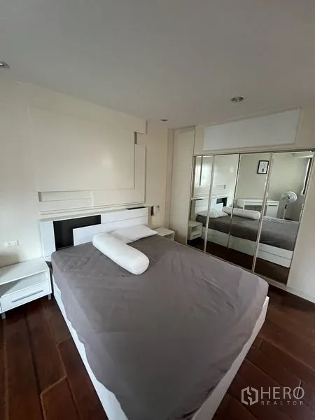 Condominium for rent - Bright master bedroom with hardwood floors, white headboard and mirrored wardrobe.