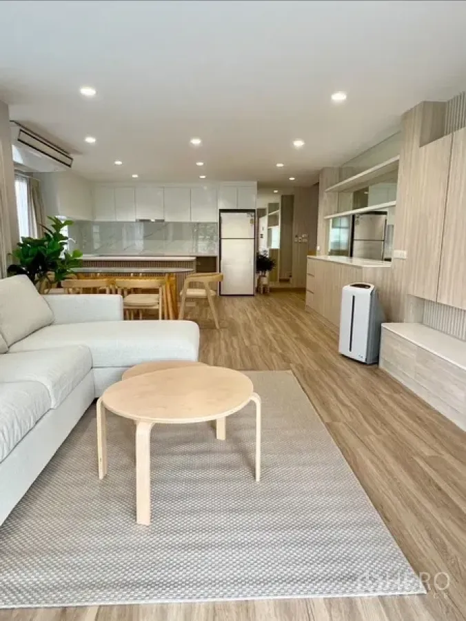 Detached House for rent in Bang Rak, Bangkok - Open-plan living room with sofa, wood floors, recessed lighting, and a bright white kitchen.