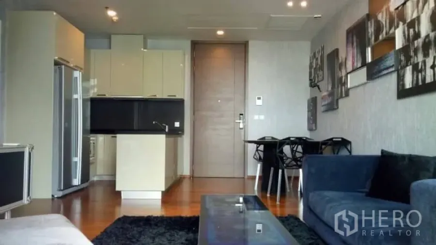 Condominium for rent or sale in Watthana, Bangkok - Open-plan living area with built-in kitchen, dining set, blue sofa and wood floors