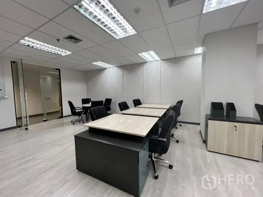办公空间 出租在Sathon, Bangkok - 共享办公桌排布，带滚轮抽屉柜，极简墙面与玻璃门营造现代感。