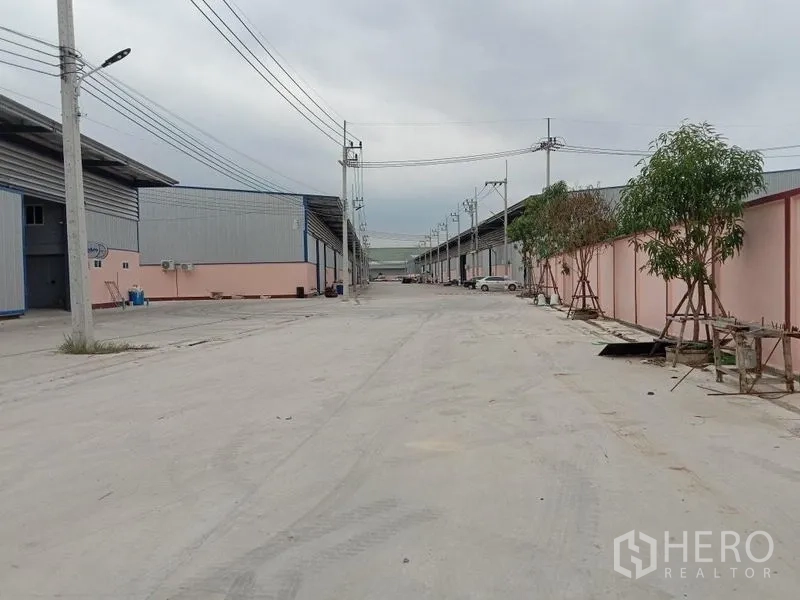 Factory for rent in Ban Phaeo, Samut Sakhon - Wide concrete access road between modern steel factory units with overhead power lines in Mueang Samut Sakhon.